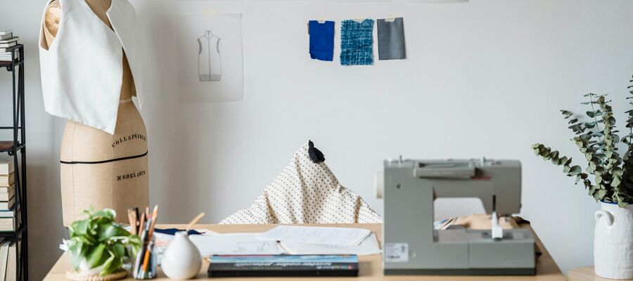 Tisch mit Nähmaschine und verschiedenen Stoffmustern, daneben Schneiderpuppe